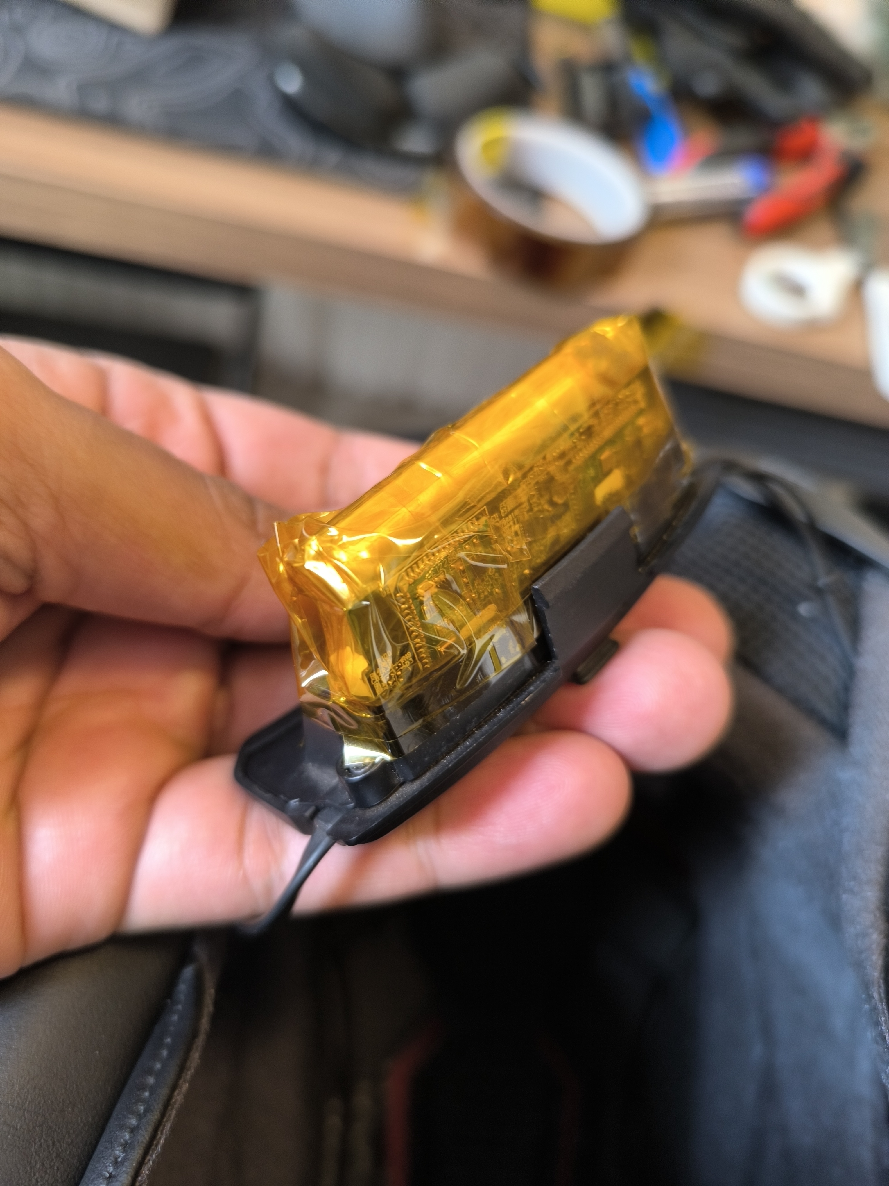 The circuit-board side of the SRL2 assembly enclosed in amber tape, held beside the remaining black plastic case.